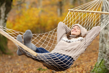 Happy woman lying on hammock in autumn forest