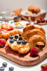 Delicious breakfast spread featuring buttery croissants topped with fresh strawberries and blueberries, served on a wooden board with butter, coffee, and fruit, creating a cozy