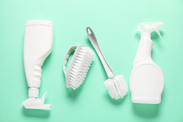 Flat lay composition with spray bottles of different cleaning products and brushes on turquoise background