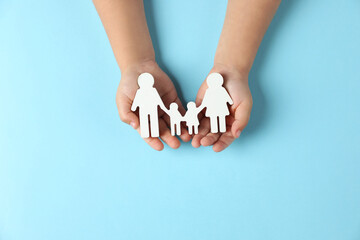 Child holding figure of family on light blue background, top view