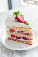 Close-up of a slice of strawberry shortcake with layers of sponge cake, whipped cream, and fresh strawberries, garnished with whipped topping, parsley, and sliced strawberries on a white plate