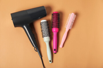 Stylish round hair brushes and hairdryer on light brown background, flat lay