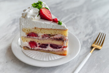 Slice of strawberry shortcake with layers of cream and fresh strawberries, garnished with whipped cream and parsley, served on a white plate with a gold fork on a marble table