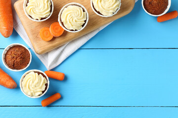 Tasty carrot muffins with fresh vegetables on light blue wooden table, flat lay. Space for text