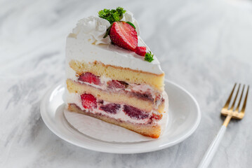 Slice of strawberry shortcake with layers of cream and fresh strawberries, garnished with whipped cream and parsley, served on a white plate with a gold fork on a marble table