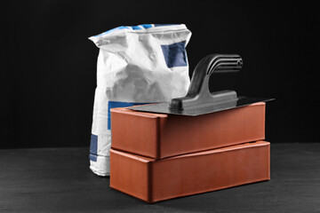 Fototapeta premium Bricks, bag of cement and construction tool on black table