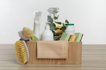 Eco-friendly cleaning products, supplies and eucalyptus branches in crate on wooden table