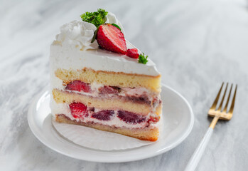 Slice of strawberry shortcake with layers of cream and fresh strawberries, garnished with whipped cream and parsley, served on a white plate with a gold fork on a marble table