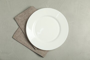 Napkin and empty plate on grey table, top view