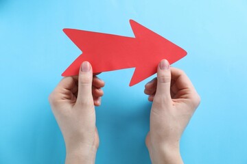 Woman with paper arrow on light blue background, top view