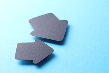 Two black paper arrows on light blue background, closeup