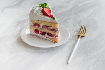 Slice of strawberry shortcake with layers of cream and fresh strawberries, garnished with whipped cream and parsley, served on a white plate with a gold fork on a marble table