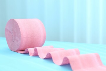 Pink toilet paper roll on light blue background, closeup. Space for text