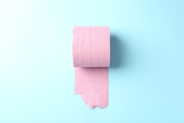Pink toilet paper roll on light blue background, top view