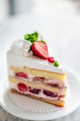 Close-up of a slice of strawberry shortcake with layers of sponge cake, whipped cream, and fresh strawberries, garnished with whipped topping, parsley, and sliced strawberries on a white plate