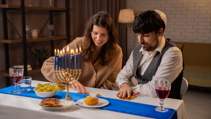 Jewish couple preparing for traditional hanukah celebrations, man and woman sitting at table, enjoying dinner and playing game, positive expression.