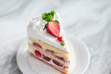 Close-up of a slice of strawberry shortcake with layers of sponge cake, whipped cream, and fresh strawberries, garnished with whipped topping, parsley, and sliced strawberries on a white plate