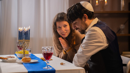 Jewish couple preparing for traditional hanukah celebrations, man and woman sitting at table, enjoying dinner and playing game, positive expression.