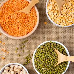 An assortment of legume products: chickpeas, mung beans, lentils, peas, beans in bowls on a cloth, burlap. Top view. Healthy nutrition, vegetarianism.