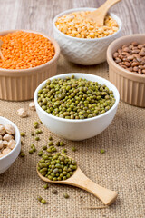 An assortment of legume products: chickpeas, mung beans, lentils, peas, beans in bowls on a cloth, burlap. Healthy nutrition, vegetarianism.
