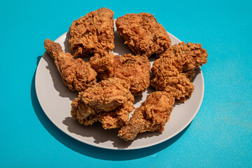 A plate of crispy fried chicken pieces placed on a neutral plate against a bright blue background, showcasing golden-brown texture and rich detail. Perfect for food photography