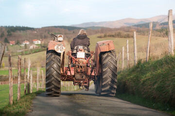 Woman farmer driving old red tractor on a country road near farm and mountains, celebrating international workers' day