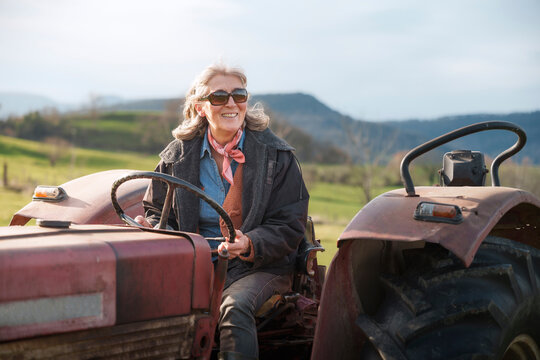 Senior farmer woman driving a tractor in a field, celebrating international workers' day