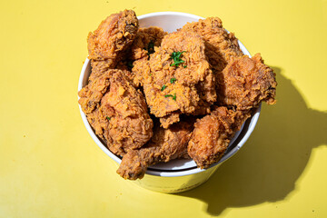 A bucket filled with crispy golden-brown fried chicken pieces placed on a vibrant red and yellow background, highlighting its crunchy texture. Perfect for fast food, takeout, or comfort food visuals