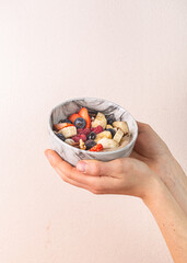 Fresh fruit bowl held in hand featuring strawberries, blueberries, bananas, and raspberries,...