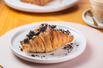 Delicious chocolate croissant topped with crushed cookies served on a white plate in a cozy café setting, perfect for dessert lovers and food enthusiasts, indulgent pastry concept
