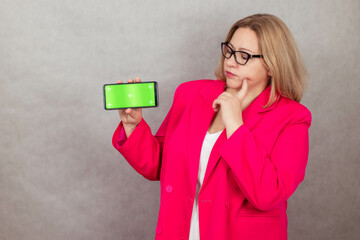 Thoughtful attractive plus size woman staring at green screen smartphone, holding one hand to her face. Copy space