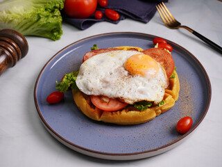Fresh waffles with fried eggs, lettuce, tomatoes and served for breakfast on a flat table.