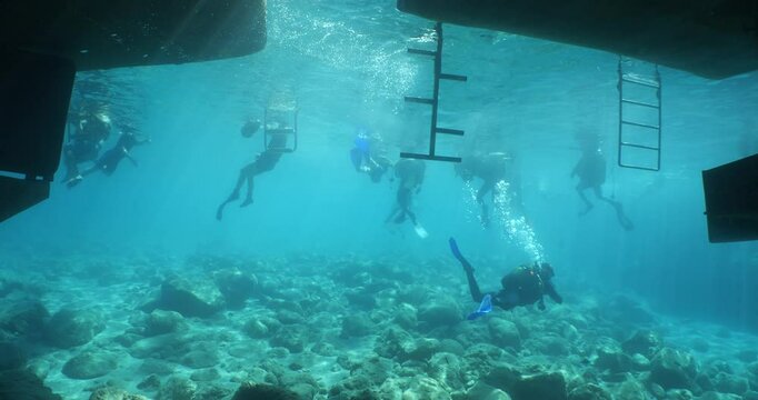 Scubadivers around the dive boat underwater with sun beams and rays