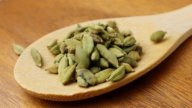 Dried green cardamom pods condiment falling down into the wooden spoon close up