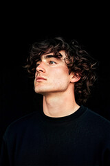 Obraz premium Dramatic portrait of a young man with curly hair wearing a black sweater, moody aesthetic 