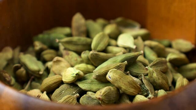 Dried green cardamom pods condiment falling down into the wooden bowl close up