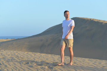 A young man going in a desert at the sunset golden hour. A man wearing white t-shirt walking along sand dune barchan in Maspalomas, Gran Canaria