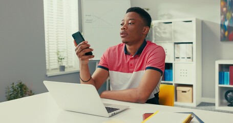 An employee of a telemarketing agency sits at a desk in front of a laptop, dials a number to a...