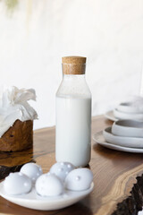Fresh milk in glass bottle on rustic background. Plate with decorative Easter eggs