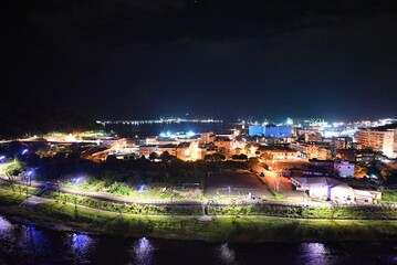 Naklejka premium Coastal City Nightscape with Illuminated Port and Reflections