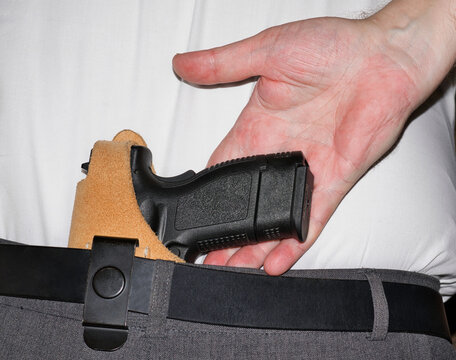 Concealed carry handgun in holster behind the back hand reaching for gun.