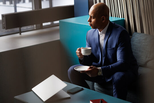 African ameican businessman drinking coffee near laptop in hotel lobby