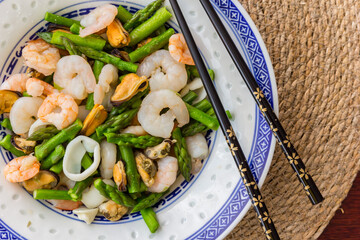 Black chopsticks on a chinese dish with mussels, prawns, squid and green asparagus