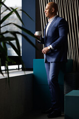 Fototapeta premium Happy African american businessman holding coffee near window in hotel lobby