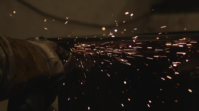 A person is cutting metal with a saw, and the sparks are flying. Concept of danger and excitement, as the sparks can be seen flying in all directions. The person is wearing a glove