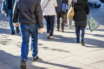 Crowd of people walking on city street in winter, wearing jackets. Concept of city life, movement, daily life, urban routine