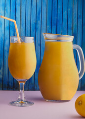 Jug and glass of a fruity drink,smoothie with a wooden blue background.