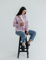 Portrait of a cute girl model in a pink checkered shirt and jeans in the studio on a white...