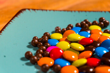 Bright colorful chocolate candies on a turquoise plate with a wooden background, perfect for food and snack photography