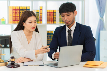 Male lawyer discussing contract documents, business woman sitting at advice table, legal consulting service and a scale with a judge's hammer placed next to it.